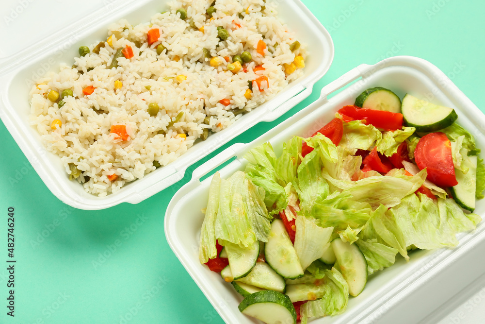 Rice with vegetables and salad mix in lunch boxes on color background, closeup