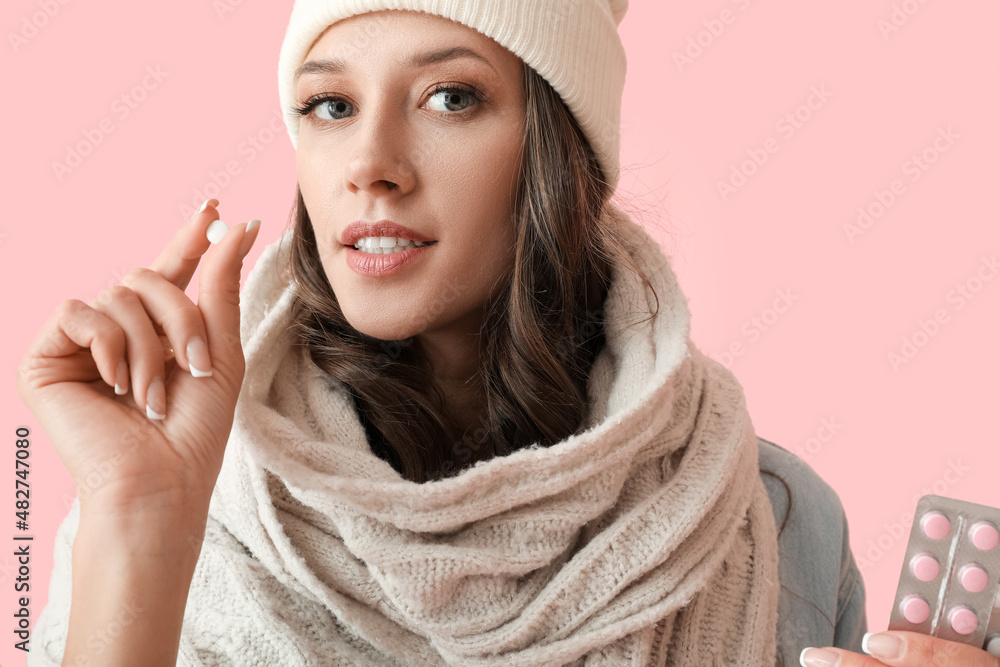 Young sick woman taking pill on color background