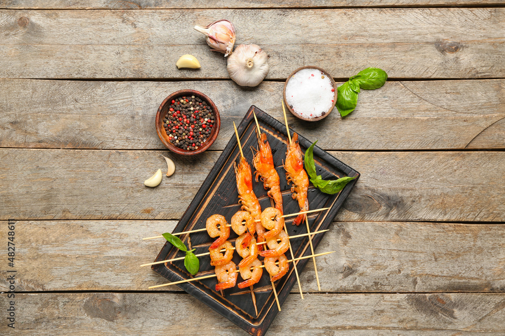 Board with grilled shrimp skewers on wooden background