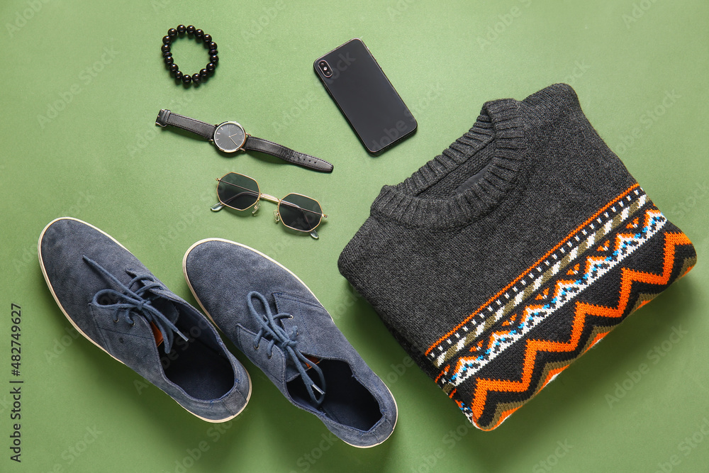 Stylish male sweater, shoes, accessories and mobile phone on green background