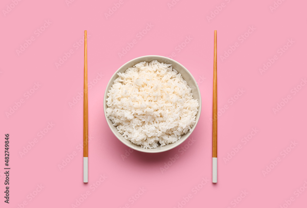 Bowl with tasty boiled rice and chopsticks on pink background