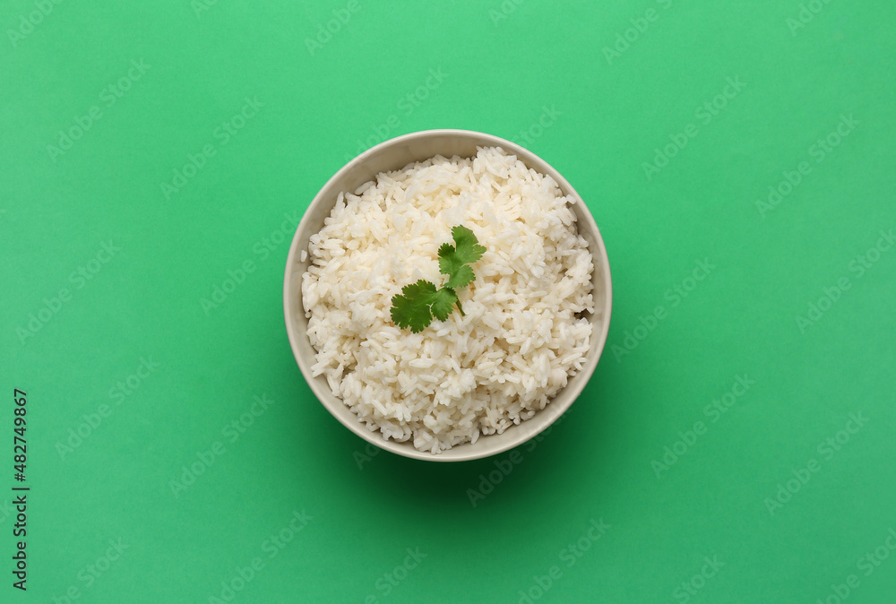 Bowl with tasty boiled rice on green background