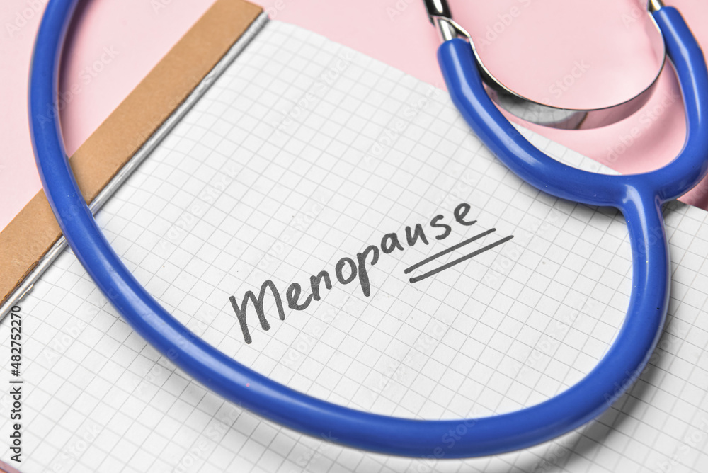 笔记本，粉红色背景，带单词MENOPAUSE和听诊器，特写