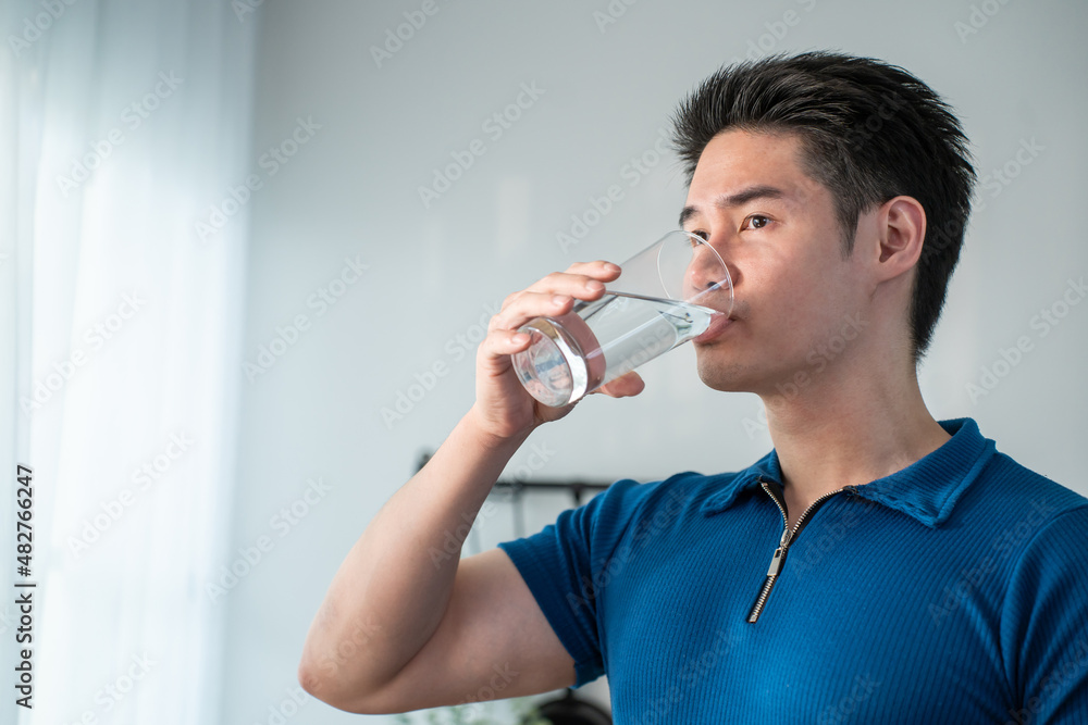 亚洲魅力男性在厨房拿着一杯水的肖像。