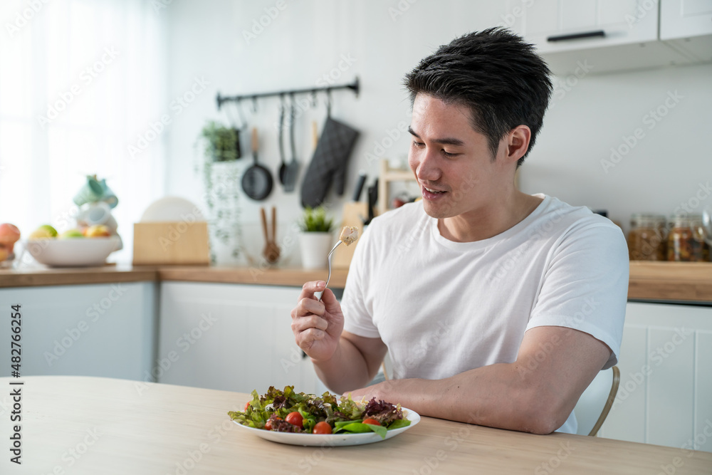 亚洲魅力英俊的男性在家的厨房里吃绿色沙拉。