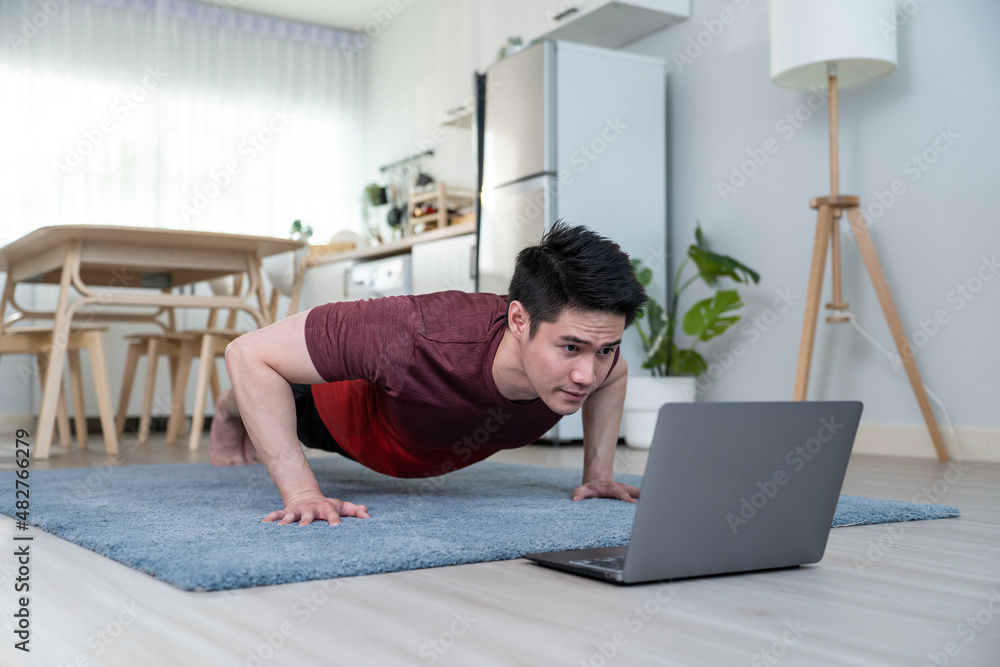 Asian handsome active young man doing push up on floor in living room.