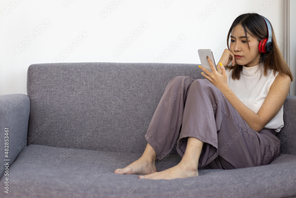 Lifestyle home life Asian woman sits using her mobile phone and listens to music on the sofa in the 