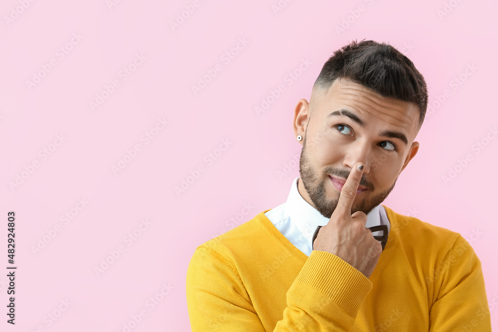 Dreamy man with stylish manicure touching nose on color background