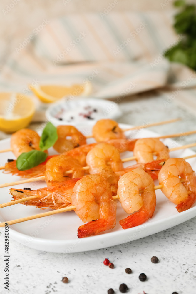 Plate with grilled shrimp skewers on light background