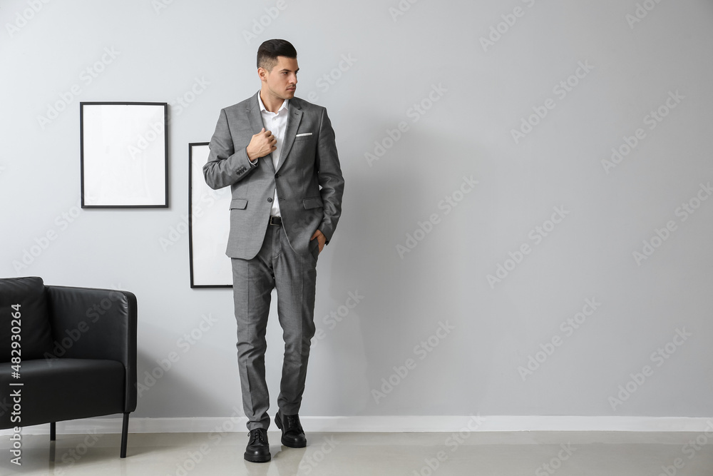 Handsome man in elegant suit near grey wall in room