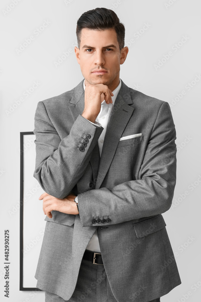 Young pensive man in elegant suit near grey wall