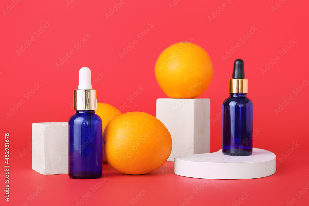 Bottles of essential oil and fresh oranges on red background