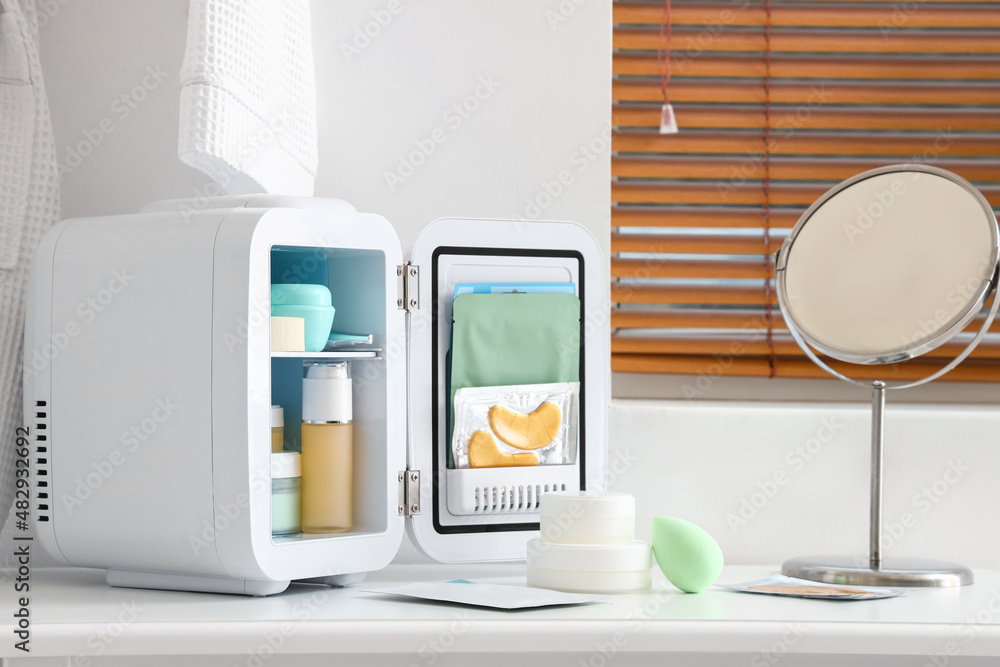 Small cosmetic refrigerator and mirror on dressing table near light wall