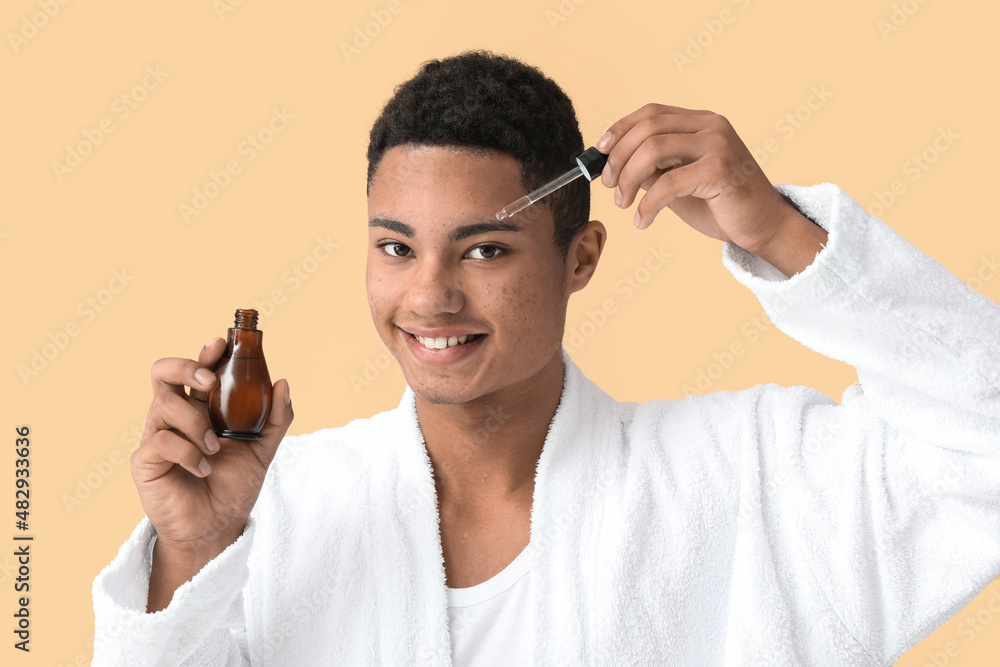 Young African-American guy with serum for skin care on color background