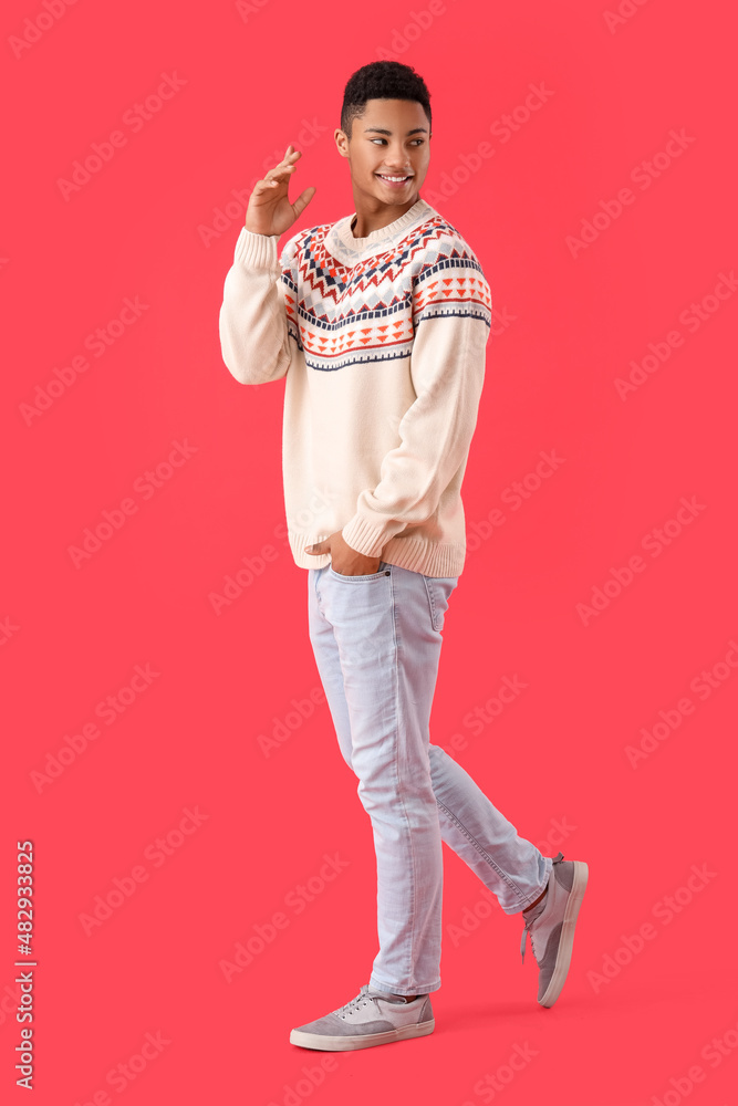 Handsome African-American guy in knitted sweater on red background