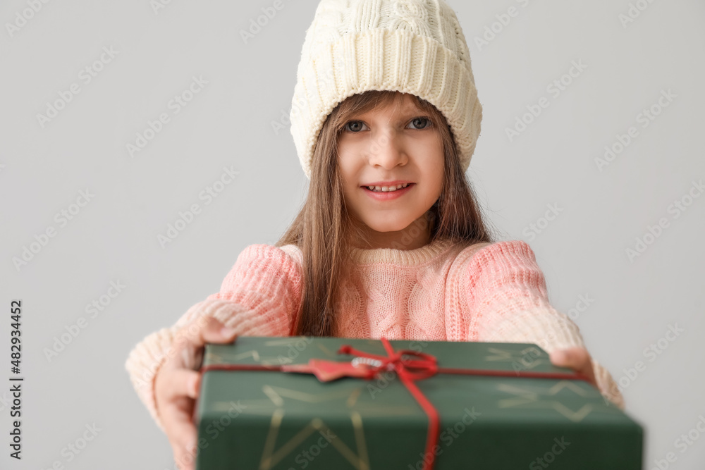 Cute little girl in winter clothes and with Christmas gift on grey background