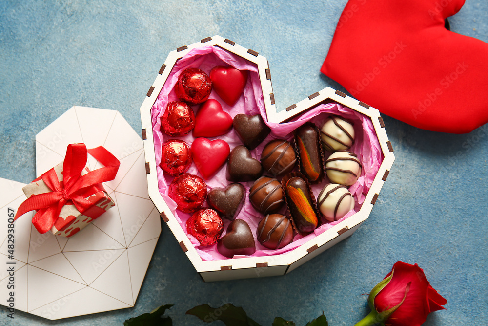 Heart shaped box with tasty chocolate candies and gift on blue background