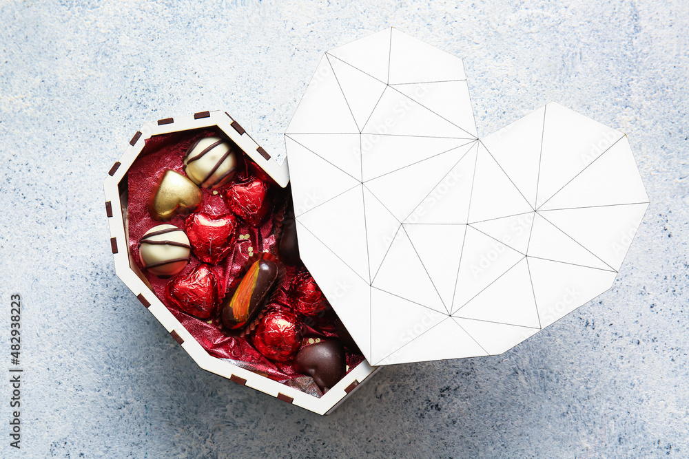 Heart shaped box with tasty chocolate candies on light background