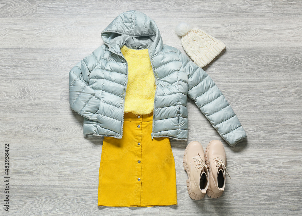 Female jacket, sweater, skirt, shoes and hat on grey wooden background