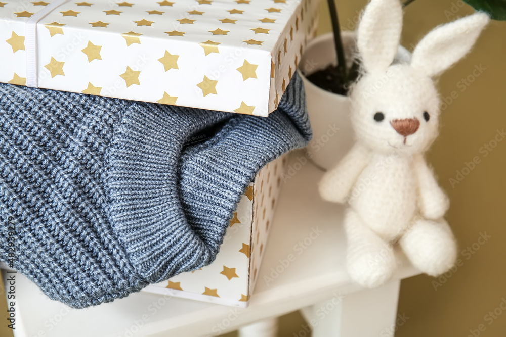 Box with knitted sweater for child and toy on stool, closeup