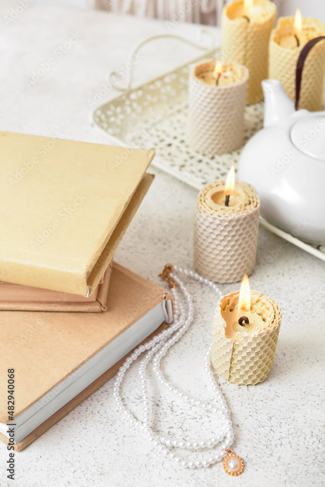 Stack of books with necklace and burning candles on white table