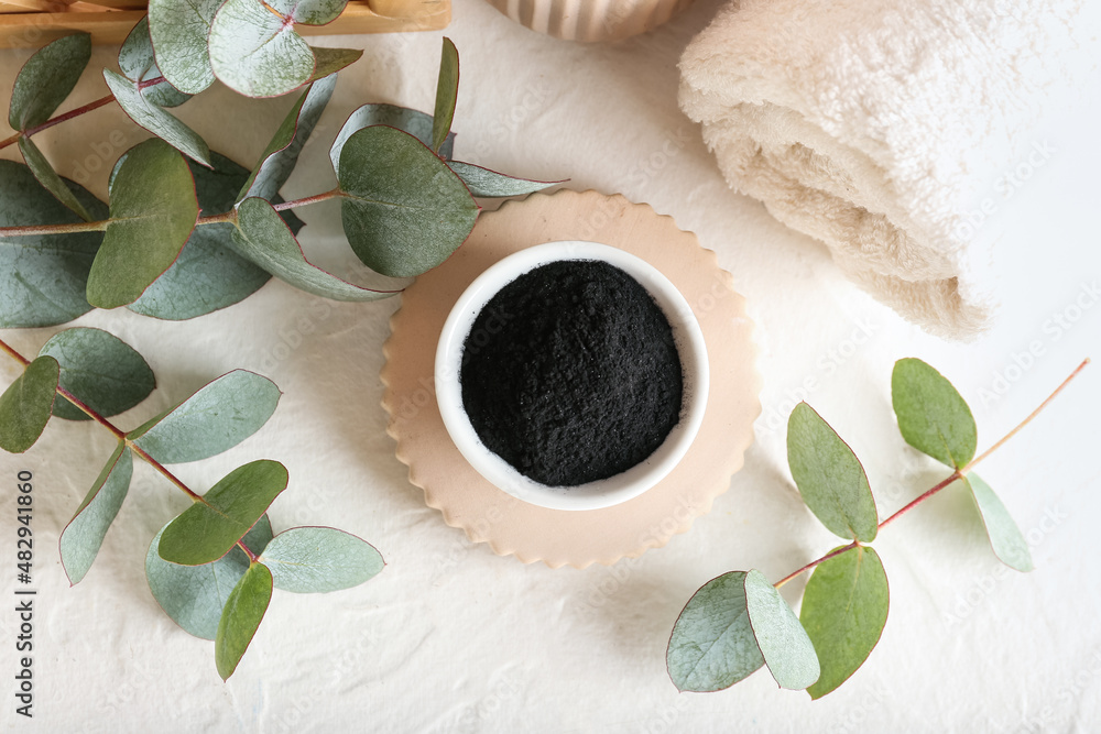 Bowl with activated charcoal tooth powder and eucalyptus branches on white background