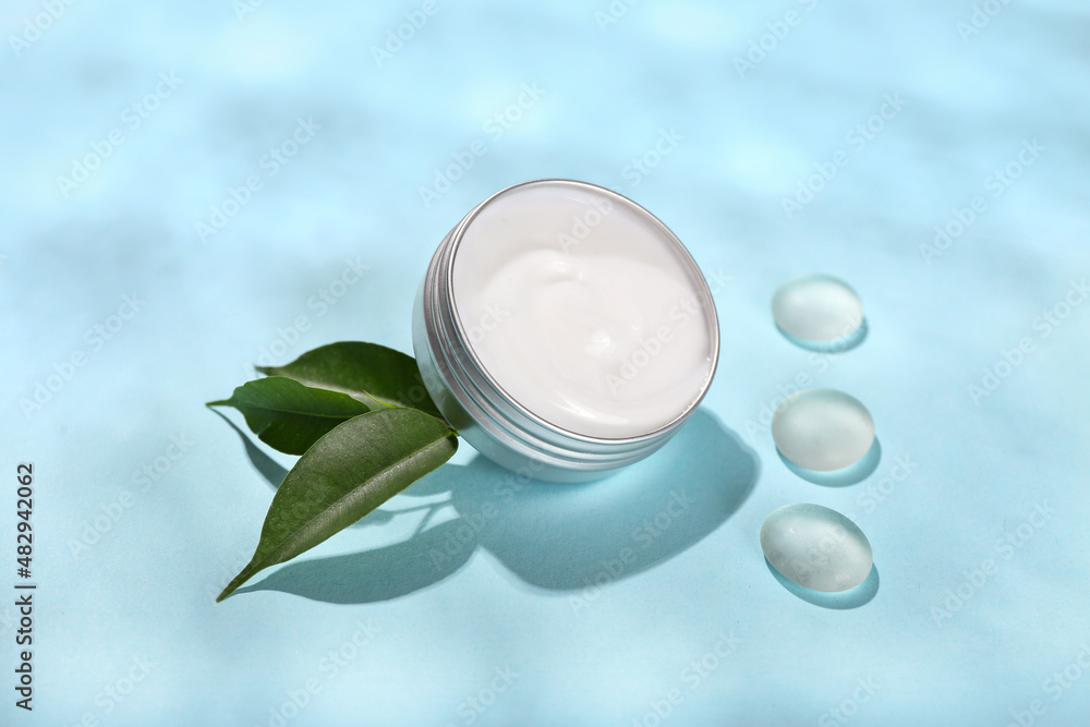 Jar with natural cosmetic cream, leaves and stones on blue background