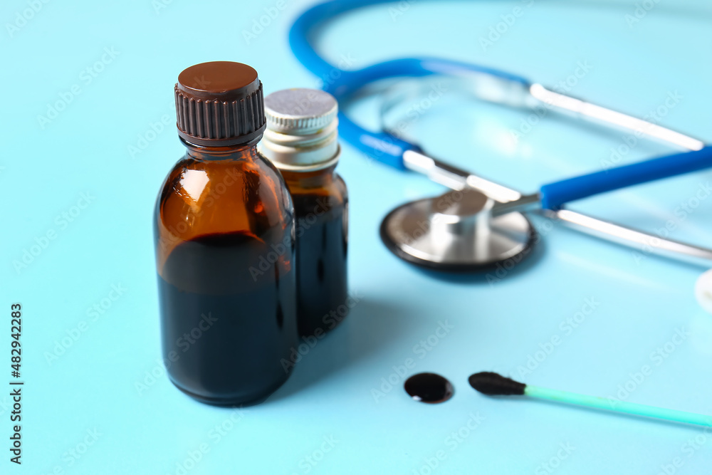 Bottles with iodine, cotton swab and stethoscope on blue background, closeup