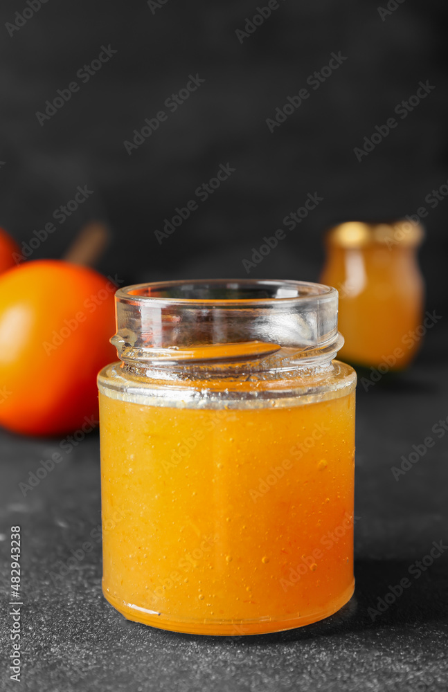 Glass jar of tasty orange jam on dark background, closeup