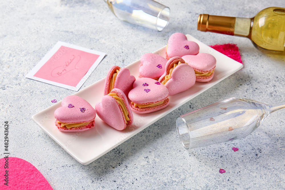 Plate with tasty heart-shaped macaroons and glass on light background