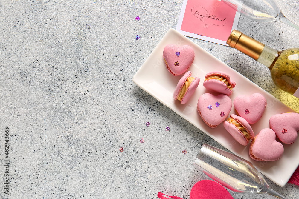 Plate with tasty heart-shaped macaroons and glass on light background