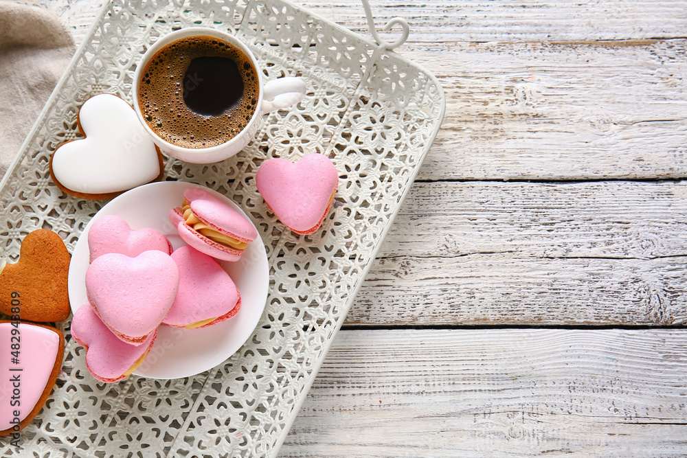 Tray with tasty heart-shaped macaroons and cup of coffee on white wooden background