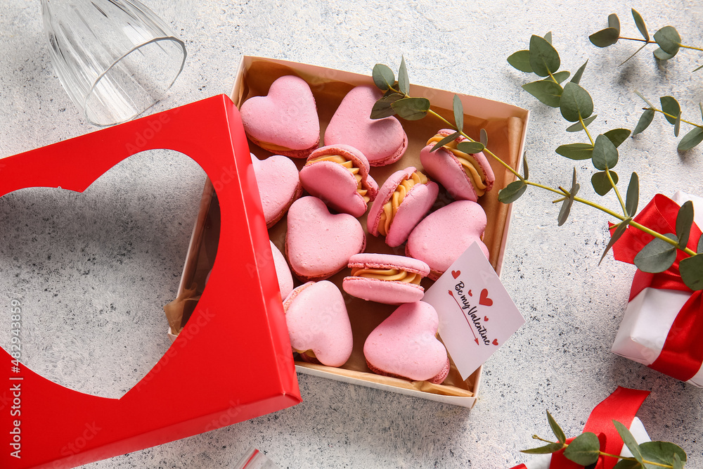 Box with tasty heart-shaped macaroons and greeting card on light background