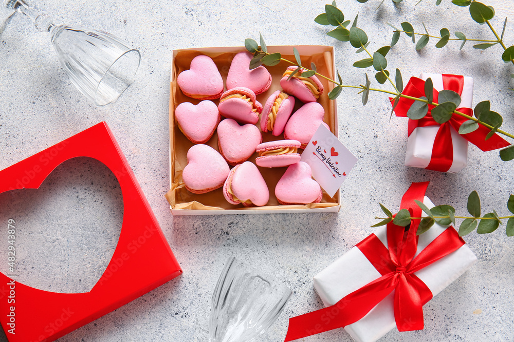 Box with tasty heart-shaped macaroons, greeting card, gifts and glasses on light background