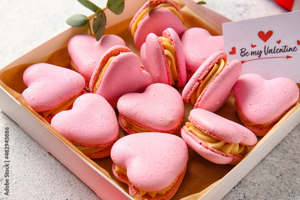 Box with tasty heart-shaped macaroons and greeting card on light background, closeup