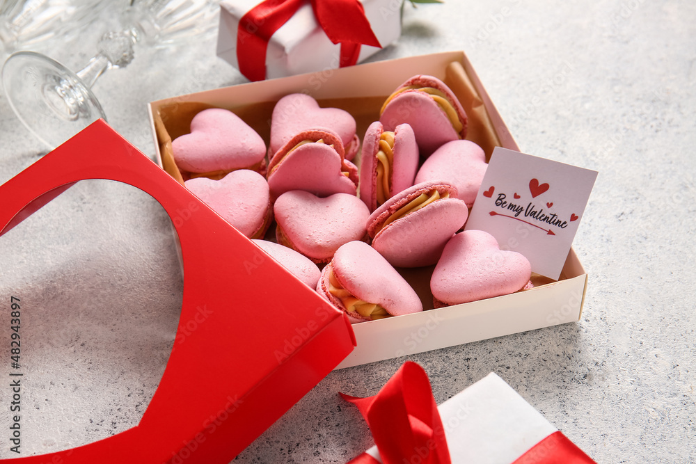 Box with tasty heart-shaped macaroons and greeting card on light background