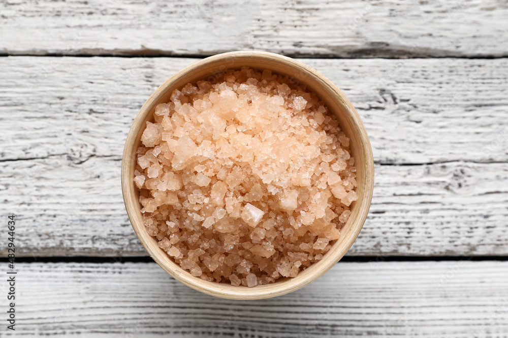 Bowl of sea salt on light wooden background