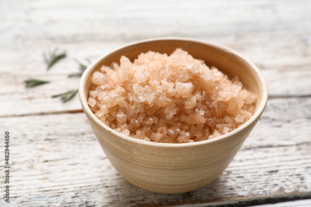 Bowl of sea salt on light wooden background, closeup