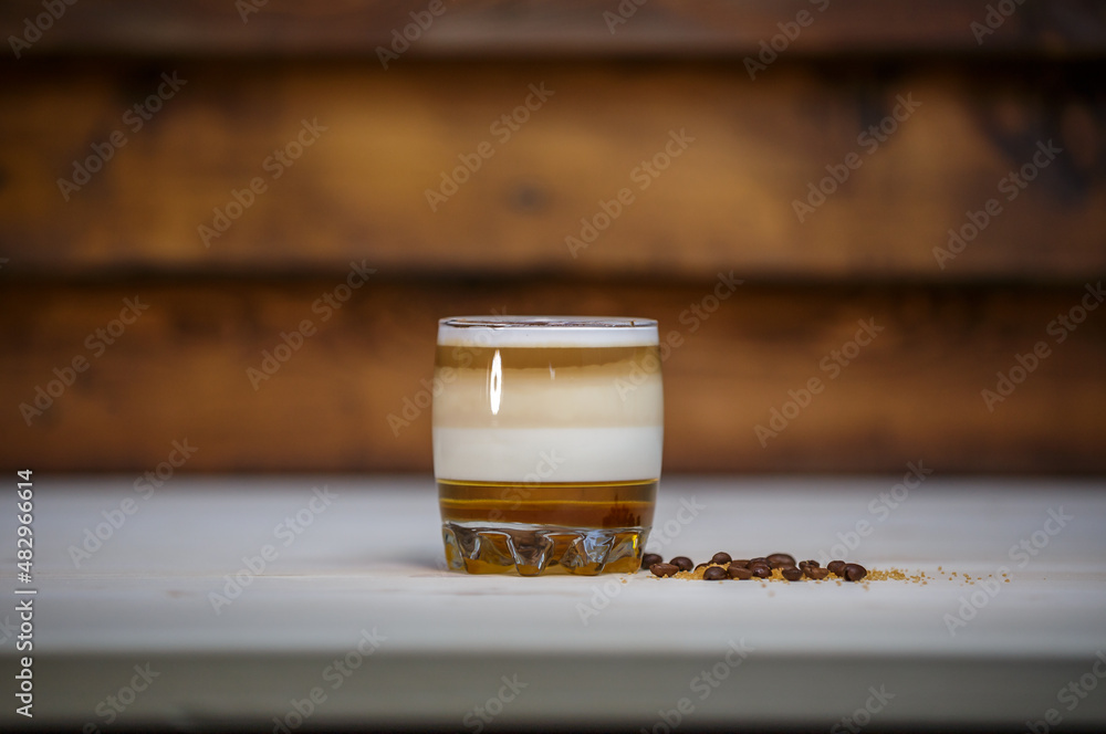 Layered coffee with cinamon in short glass on table with wood background and coffee beans