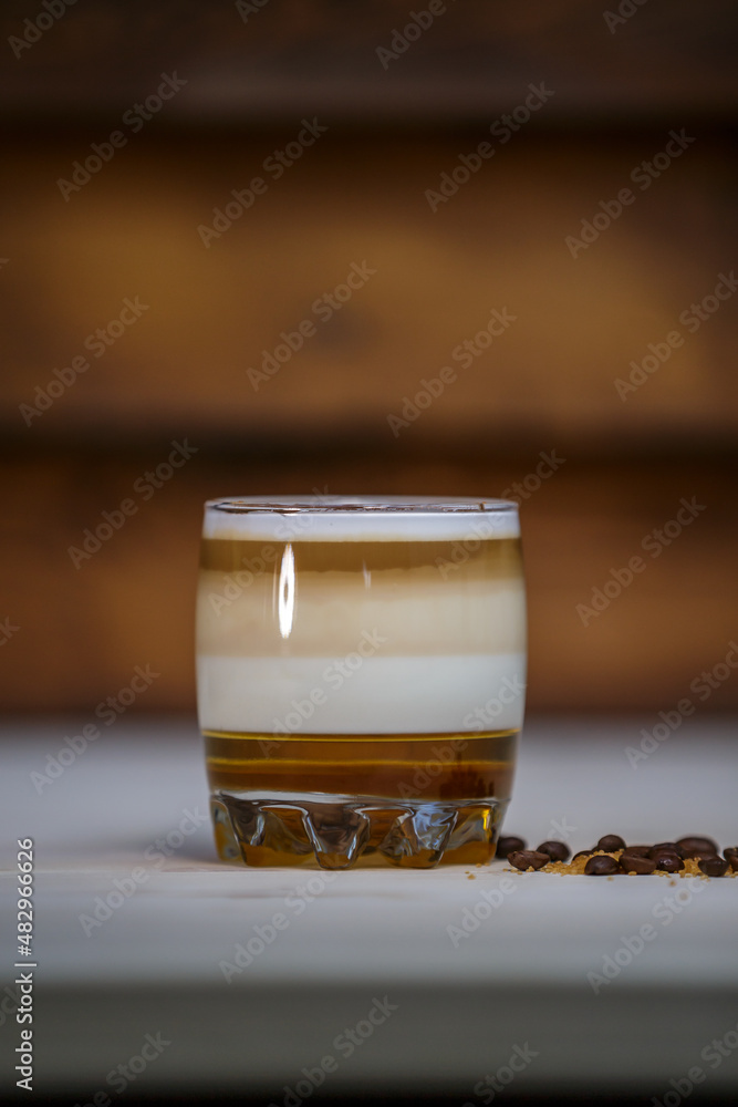 Layered coffee with cinamon in short glass on table with wood background and coffee beans