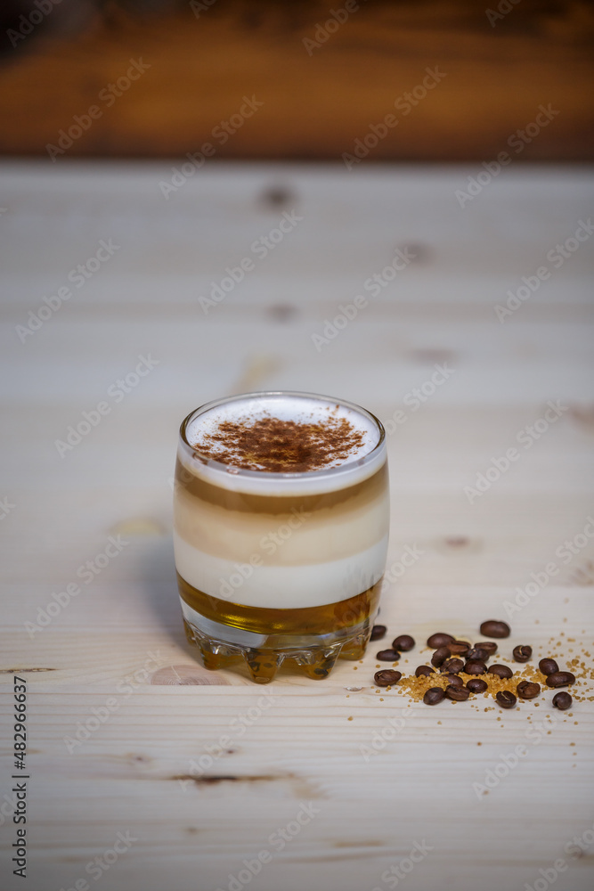 Layered coffee with cinamon in short glass from angle on table with wood background and coffee beans