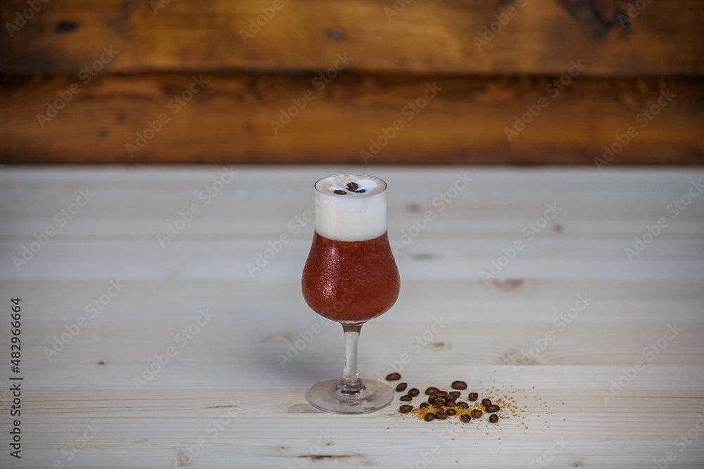 Crushed ice coffee with cinamon in brandy glass from angle on table with wood background and coffee 