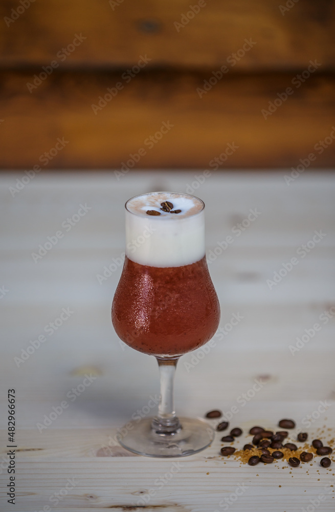 Crushed ice coffee with cinamon in brandy glass from angle on table with wood background and coffee 