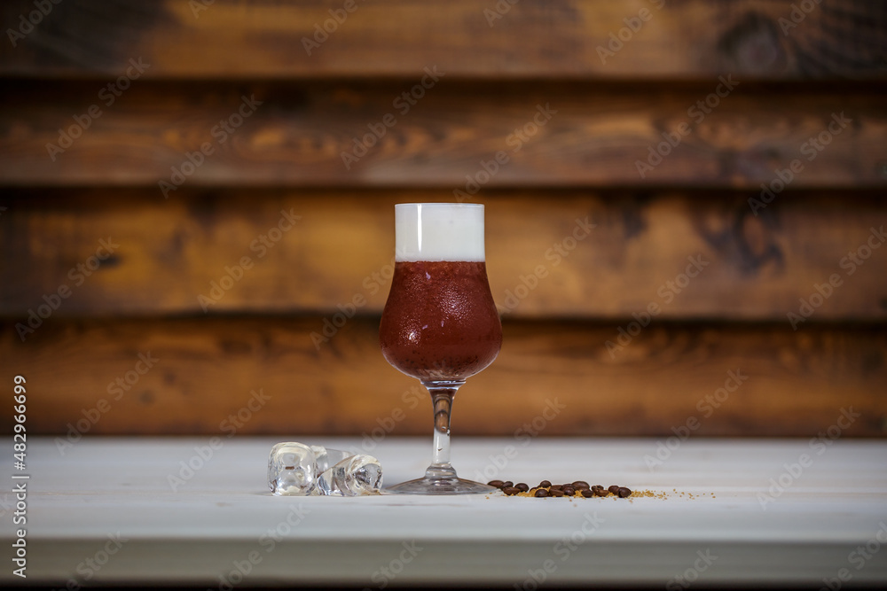 Crushed ice coffee with cinamon in brandy glass on table with wood background and coffee beans