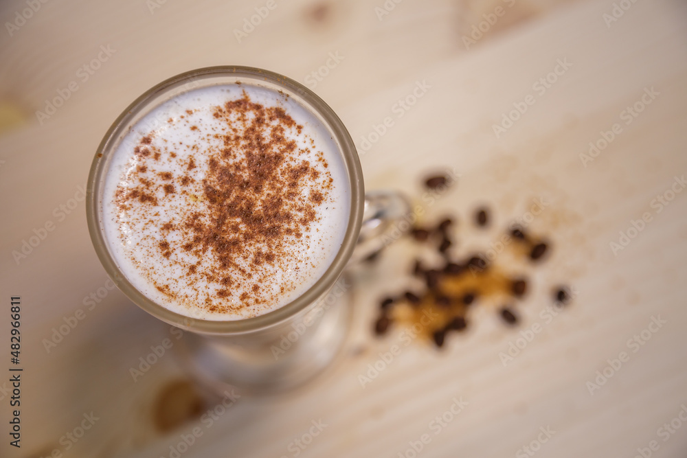 Cappucino with cinamon in tall glass from above on table with wood background and coffee beans