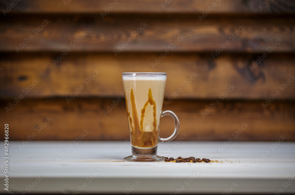 Cappucino with cinamon in tall glass on table with wood background and coffee beans