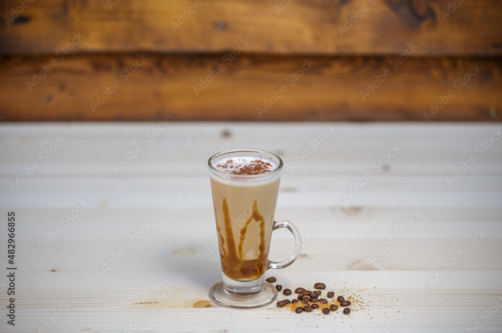 Cappucino with cinamon in tall glass on table with wood background and coffee beans