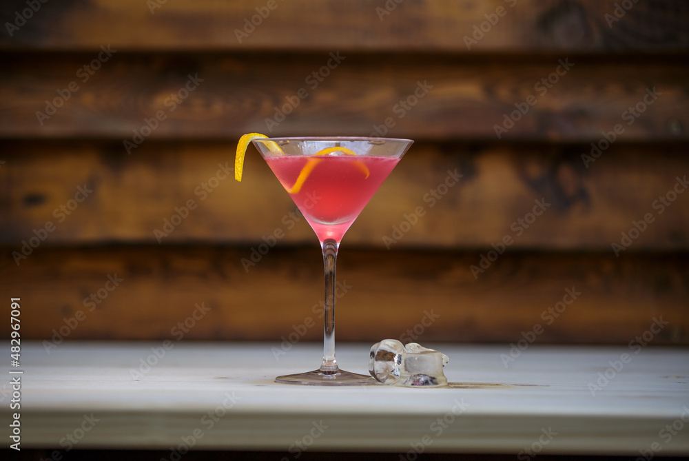 Fresh cosmopolitan martini with lemon twist on table with wood background