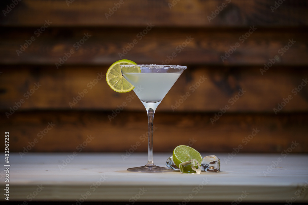 Fresh cold martini cocktail glazed and crushed ice with lime garnish on table with wood background