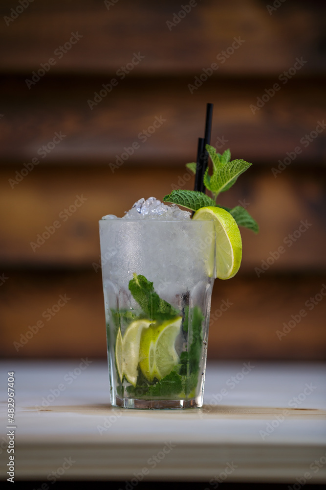 Fresh cold Mojito cocktail with lime and mint and crushed ice on table with wood background